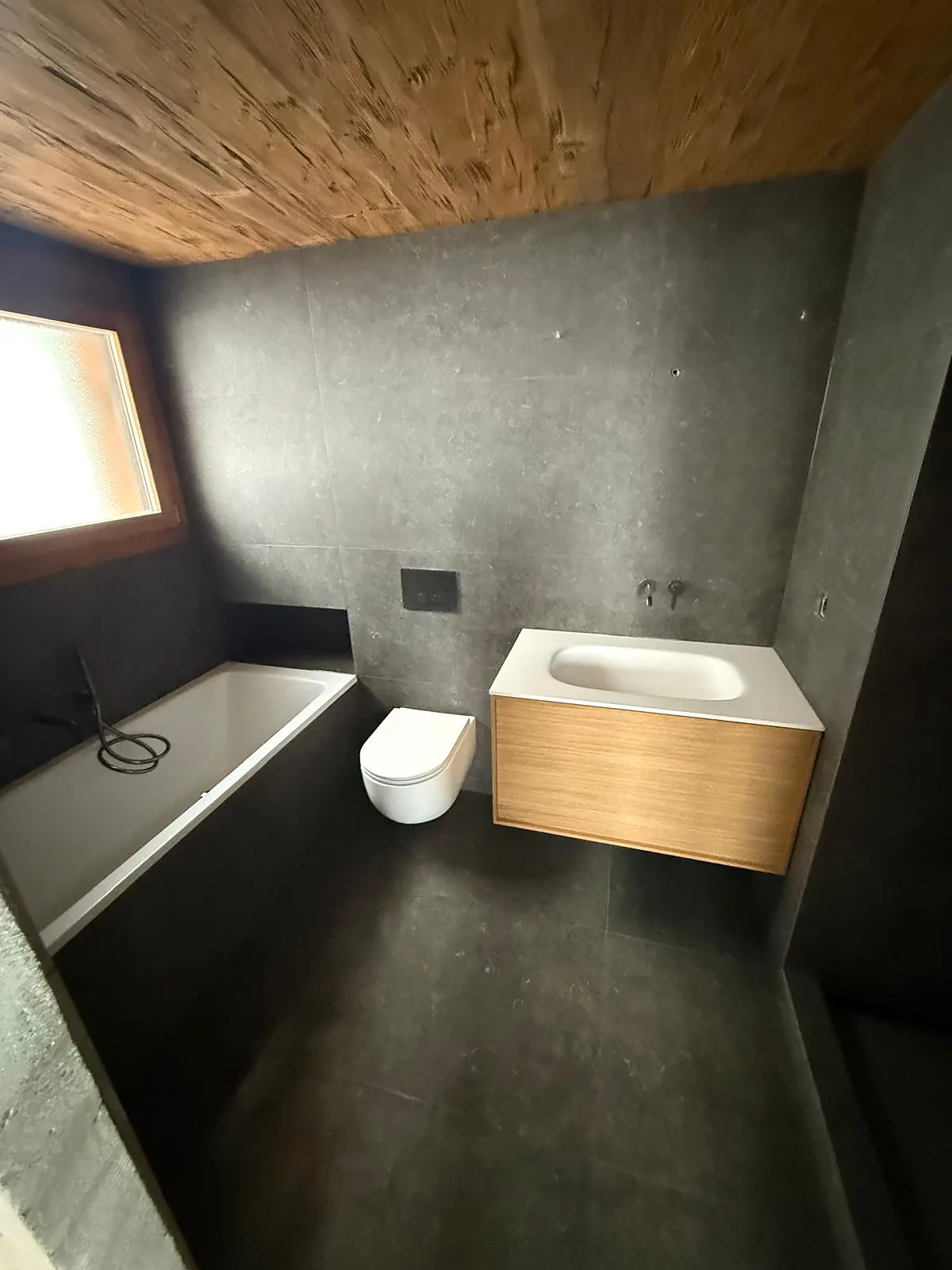 Salle de bain carrelée en anthracite sous un plafond en bois, meuble vasque en chêne