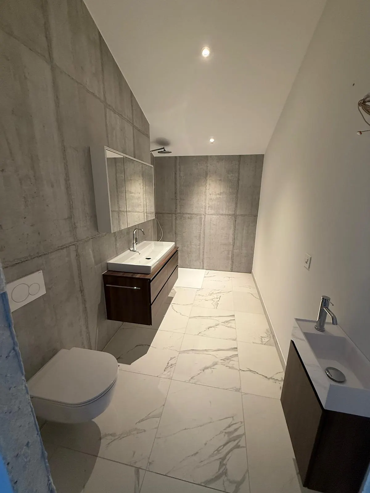 Salle de bain avec sol en grand format aspect marbre blanc et murs aspect béton